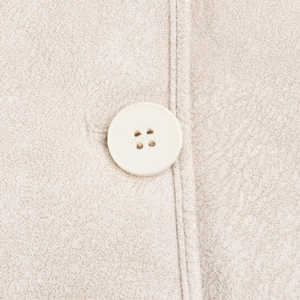 Close-up of a white four-hole button on textured beige faux suede fabric stitching