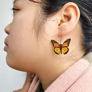 Detailed view of an orange and black monarch butterfly wing earring worn on the ear