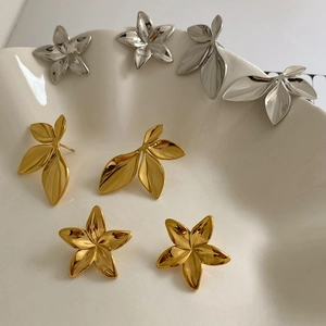 Detailed view of leaf and flower earrings on a white ceramic tray in gold and silver
