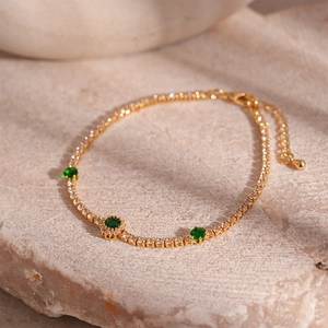Detailed close-up of golden tennis bracelet with green emerald zircons and white crystals
