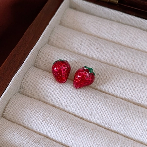 Close-up of strawberry enamel stud earrings featuring red texture and green leaves