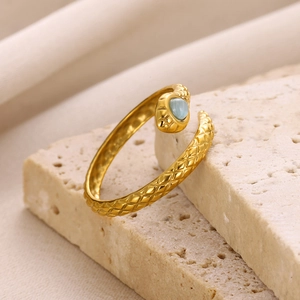 Close-up of golden snake ring with light blue gemstone and textured scale details