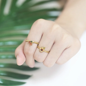 Chic gold rings featuring colorful zirconia cherry and apple fruit charms on model's hand