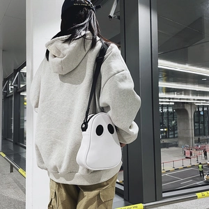 Rear view of a white ghost-shaped crossbody bag worn by a model in a modern urban setting