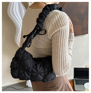 Detail of black quilted shoulder bag featuring ruffled straps and decorative bows