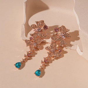 Detailed macro view of rose gold butterfly earrings with pink crystals and teal teardrop stones