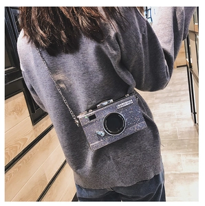 Sparkly silver camera-shaped crossbody bag with chain strap worn by a model