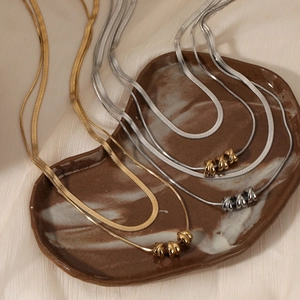 Double layered gold and silver snake chain necklace with spiral beads on a ceramic plate