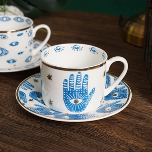 Detail of ceramic coffee cup with Hamsa hand eye motif and gold-rimmed edges on wood