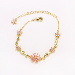 Detailed close-up of pink cherry blossom bracelet with gold chain and green leaf accents