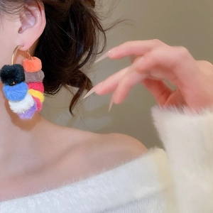 Close-up of colorful plush pom-pom hoop earrings worn by a model for a luxury fashion look