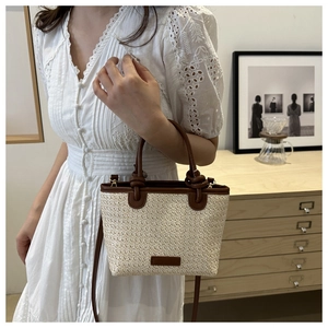 Detail of woven straw handbag with brown leather trim and knotted handles on model