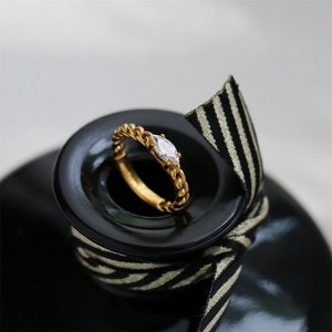 Macro detail of a 18K gold plated chain ring featuring a marquise-cut zircon on black ceramic