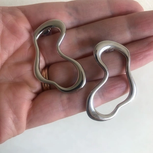 Detailed view of oversized abstract silver-tone hollow earrings held in hand