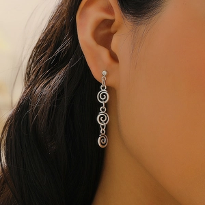 Gros plan de boucles d'oreilles spirales argentées avec trois éléments métalliques reliés