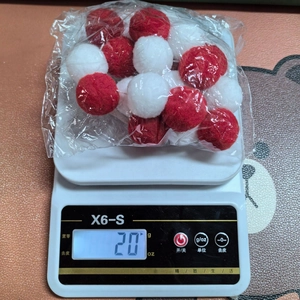 Detailed view of 20g red and white felt pom-pom garland on a digital weighing scale