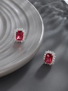 Macro shot of silver stud earrings with emerald-cut red stone and white crystal halo