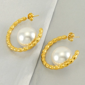 Detail of gold-plated stainless steel hoop earrings with large white pearls on textured fabric