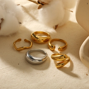 Minimalist 18K gold and silver waterdrop rings set on a textured beige fabric background