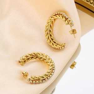 Elegante goldene gedrehte C-Ohrringe mit Zirkonia-Steinen auf glänzendem Satin-Stoff