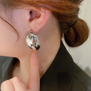 Detailed close-up of a silver irregular bean earring with a polished mirror finish on model