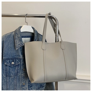 Détail d'un grand sac cabas gris avec coutures verticales suspendu à un support métallique