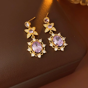 Close-up of vintage gold floral earrings with purple zircon on brown leather box