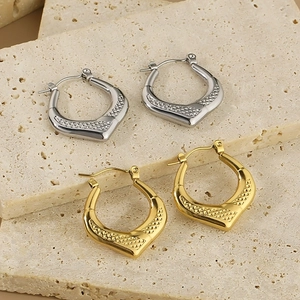 Macro detail of geometric hoop earrings with embossed diamond patterns in gold and silver