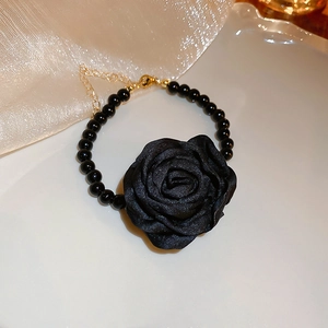 Détail d'un élégant collier ras du cou camélia en tissu noir avec chaîne de perles