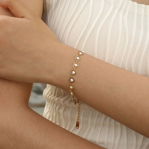 Detailed close-up of a golden heart bracelet with white enamel on a model's wrist