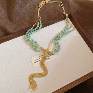 Macro detail of multilayered crystal beaded necklace with golden metal tassel on linen