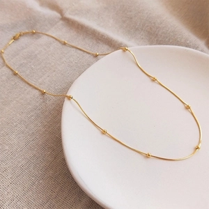 Elegant 18K gold bead snake chain necklace displayed on a white ceramic plate