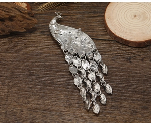 Detailed back view of silver peacock brooch with metal texture and dangling chain fringe