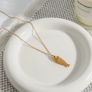 Detailed close-up of a gold fish pendant necklace with textured scales on a ceramic dish