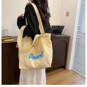 Close-up of yellow canvas tote bag showing textured fabric and blue Beach print