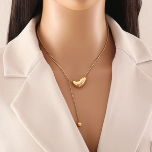Layered gold heart pendant necklace with pearl detail on a model in a beige suit
