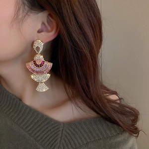 Detailed close-up of a model wearing fan-shaped gold earrings with pink and purple zircons