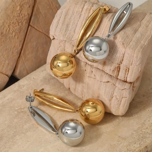 Polished gold and silver hollow sphere drop earrings on minimalist stone surface