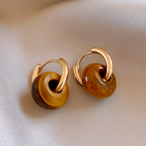 Close-up of leopard print resin earrings with golden metal ring on beige silk fabric
