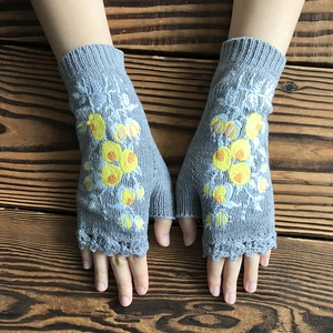 Gray knitted fingerless gloves with yellow floral embroidery on dark wood background
