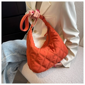 Detail of an orange quilted crescent bag worn by a model in a stylish home setting