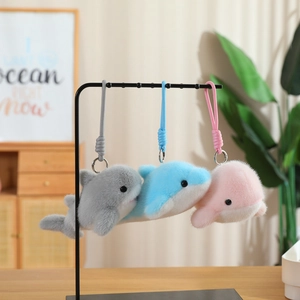Three plush dolphin keychains in grey, blue, and pink colors hanging on a metal display stand
