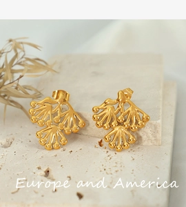 Detailed macro shot of golden pine branch stud earrings on a natural textured stone base