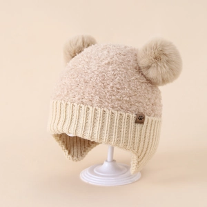 Dettaglio del cappello invernale beige per neonati con due pompon e paraorecchie in maglia