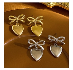 Close-up of gold and silver bow stud earrings with heart pendants in a brown bowl