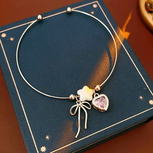 Detailed close-up of a silver open bangle with a pink heart gem and a star pendant