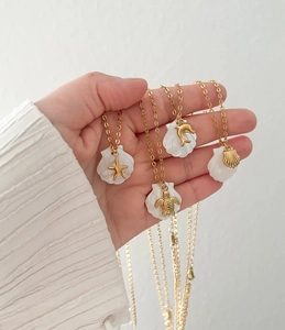 Detail of nautical pendants featuring gold starfish and turtle on white shell bases