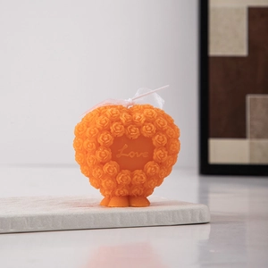 Detail of orange heart-shaped rose candle with Love engraving on a stone tray