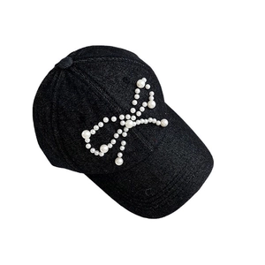 Close-up of a black denim baseball cap featuring an elegant white pearl bow design