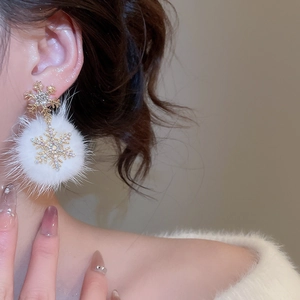 Close-up of snowflake pom-pom earrings with gold rhinestones worn by a model
